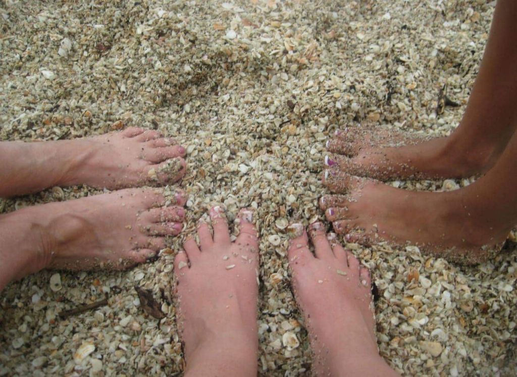 Three pairs of feet buried in the shell filled sand at playa conchal.
